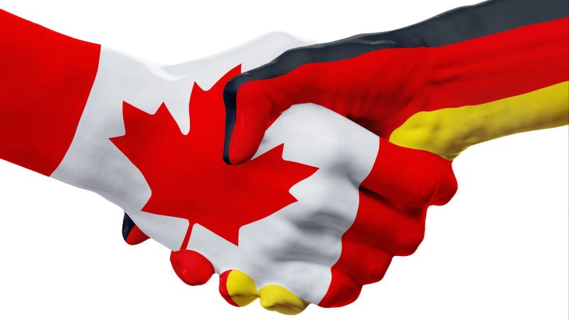 Zwei Hände reichen sich zum Handschlag, eine ist in der kanadischen Flagge, die andere in der deutschen Flagge eingefärbt. Das Bild symbolisiert die enge Partnerschaft zwischen Kanada und Deutschland.