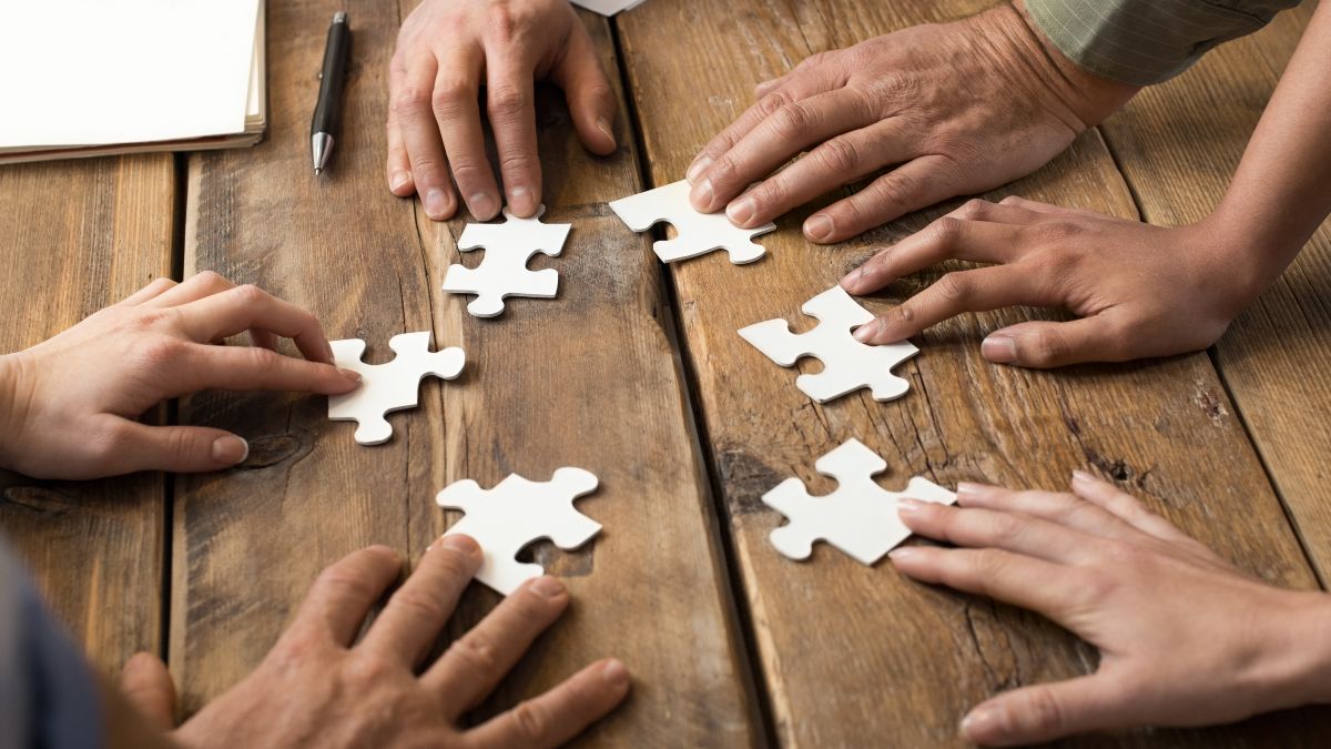 Mehrere Hände eines internationalen Teams fügen Teile eines Puzzles zusammen.