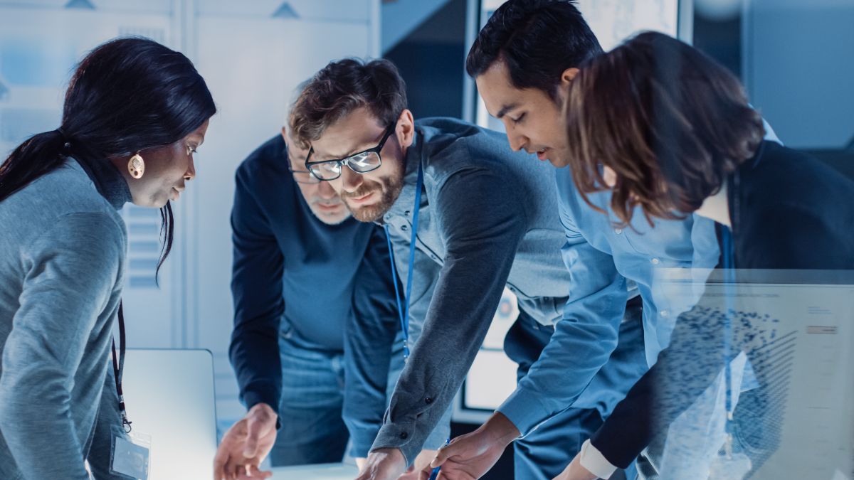 Ein internationales Forschungsteam arbeitet konzentriert an einem Tisch, auf dem verschiedene Plänen ausliegen